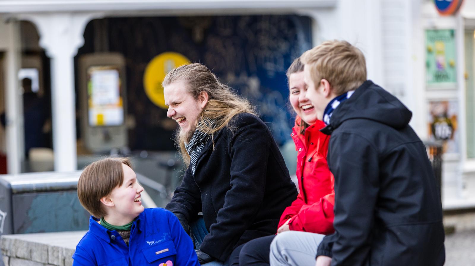 fire ungdom og voksne sitter sammen utendørs, prater og ler.